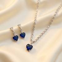 Heart-shaped blue gemstone earrings and necklace on a beige fabric background