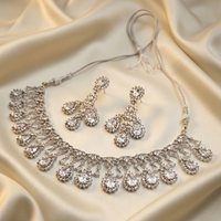 Silver necklace and earrings set on a beige fabric background
