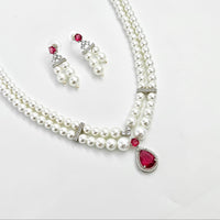 Pearl necklace with red gemstones and matching earrings on a white background