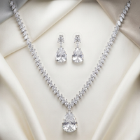 Silver necklace and earrings set on a white cushion with a black light fixture above.