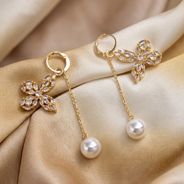 Gold earrings with floral designs and pearl drops on a beige fabric background