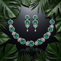 Emerald necklace and earrings on a dark background with green leaves
