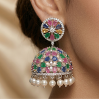 Multicolored gemstone earring with pearl drop worn by a person on a beige background