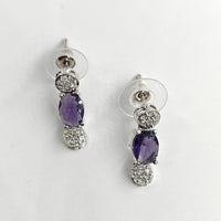 Pair of silver earrings with purple gemstones on a white background