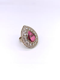 Ring with a pink teardrop-shaped gemstone and diamond-studded band on a white background
