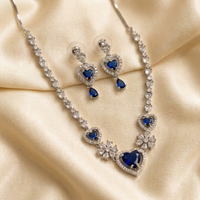 Jewelry set with necklace and earrings featuring blue heart-shaped stones on a beige fabric background