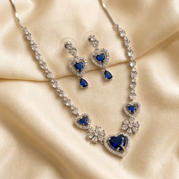 Jewelry set with necklace and earrings featuring blue heart-shaped stones on a beige fabric background