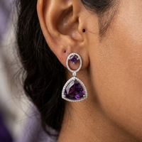 Close-up of a woman wearing purple gemstone earrings with a blurred background