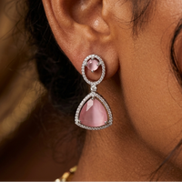 Close-up of an ear wearing a pink teardrop earring with a blurred background