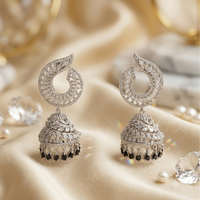 Silver earrings with intricate designs on a soft beige fabric background