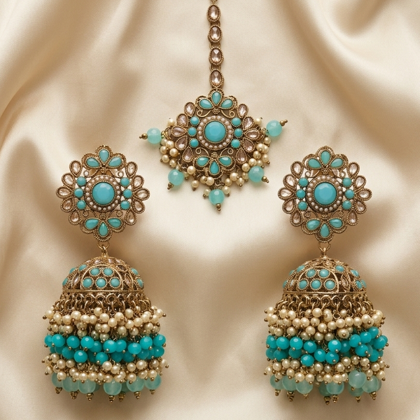Ornate earrings with turquoise stones and pearl-like beads on a beige fabric background