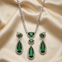 Jewelry set with emerald green teardrop earrings and necklace on a beige fabric background