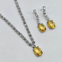 Jewelry set with yellow gemstones and silver chains on a light gray background