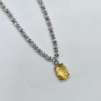 Necklace with a yellow gemstone and diamond-like stones on a light gray background