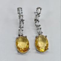 Pair of yellow gemstone earrings with silver accents on a light gray background